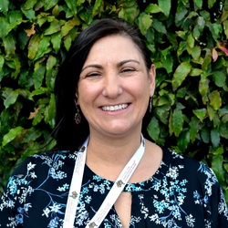 A picture of Athena Warren, our Assistant Camp Coordinator. She is smiling with a hedge in the background.